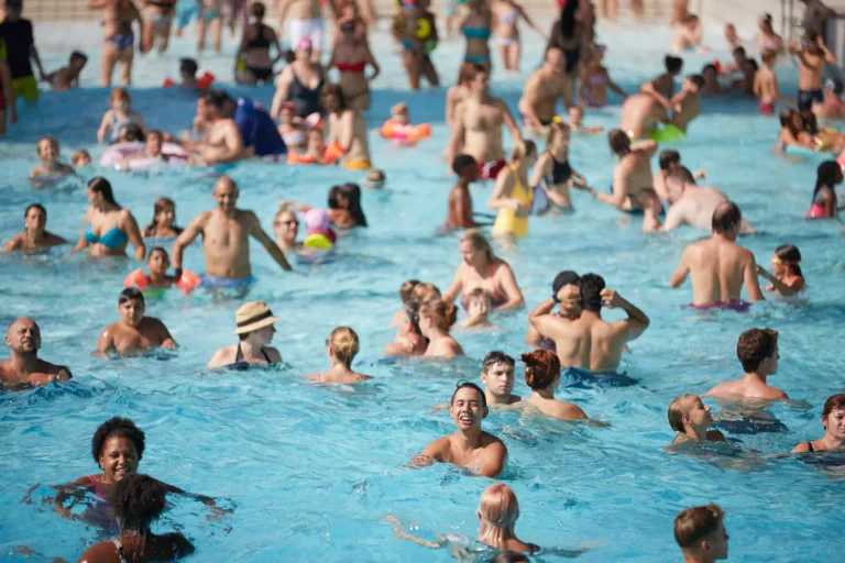 Ein buntes Gewimmel aus Kindern und Erwachsenen tummelt sich fröhlich im türkisblauen Freibadbecken des Gänsehäufels; Sonnenlicht glitzert auf den kleinen Wellen und fängt das lebhafte Sommergefühl ein.